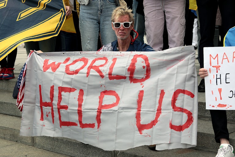Ryan Routh wears sunglasses and holds a large white banner that reads "World Help Us."
