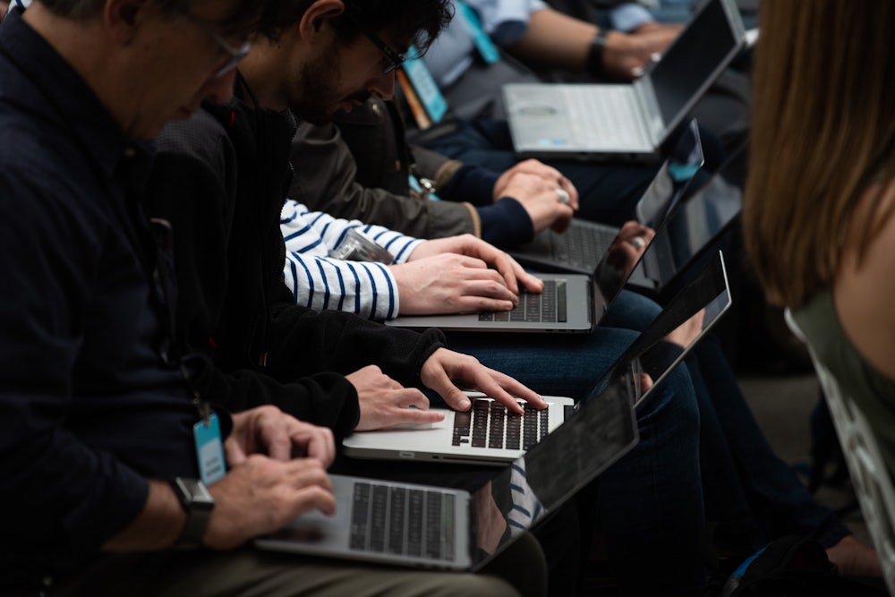 Writers type on laptops side by side