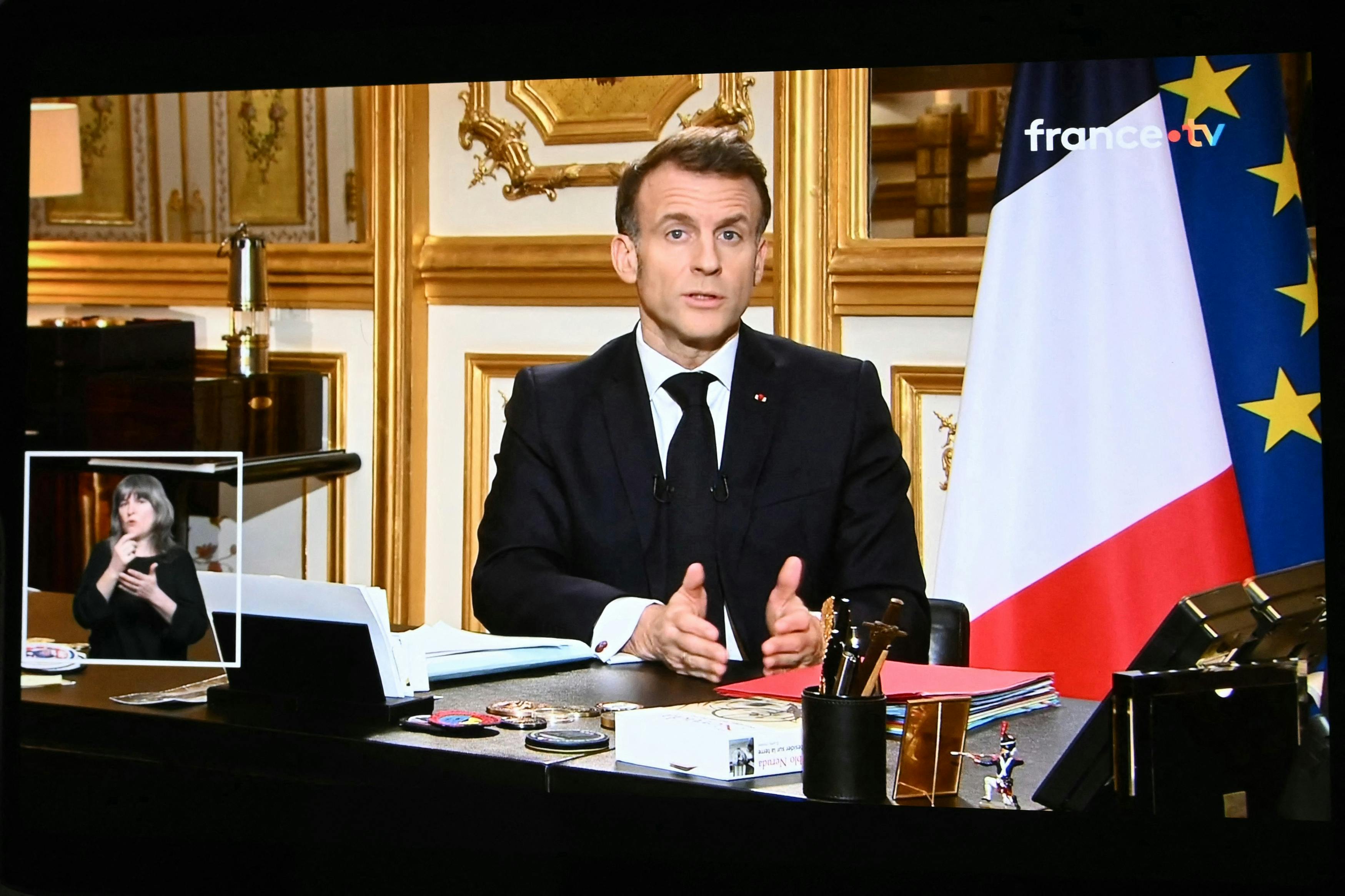 A screen displays French President Emmanuel Macron sitting at a desk and speaking