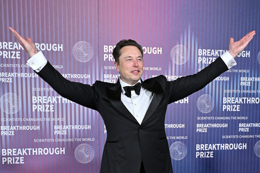 Elon Musk stands with his arms raised.
