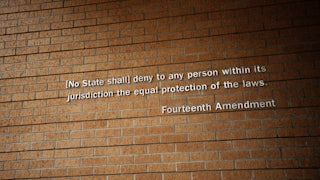 Part of the Fourteenth Amendment as posted on the wall of Little Rock Central High School National Historic Site in Little Rock, Arkansas. The text reads '(No State shall) deny to any person within its jurisdiction the equal protection of the laws.'
