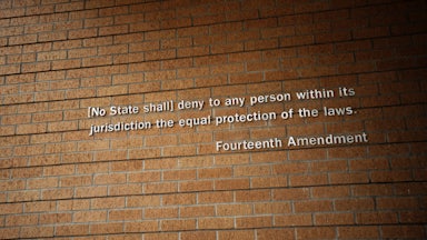 Part of the Fourteenth Amendment as posted on the wall of Little Rock Central High School National Historic Site in Little Rock, Arkansas. The text reads '(No State shall) deny to any person within its jurisdiction the equal protection of the laws.'