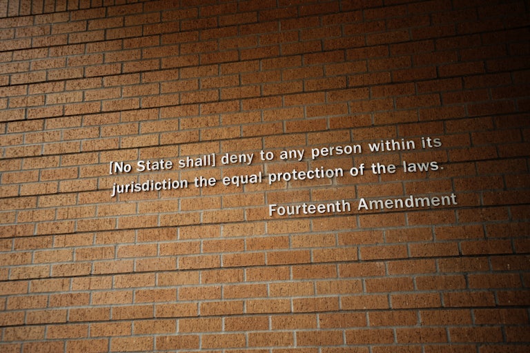 Part of the Fourteenth Amendment as posted on the wall of Little Rock Central High School National Historic Site in Little Rock, Arkansas. The text reads '(No State shall) deny to any person within its jurisdiction the equal protection of the laws.'