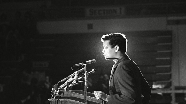 A black-and-white photograph of Julian Bond standing before a lectern equipped with microphones.