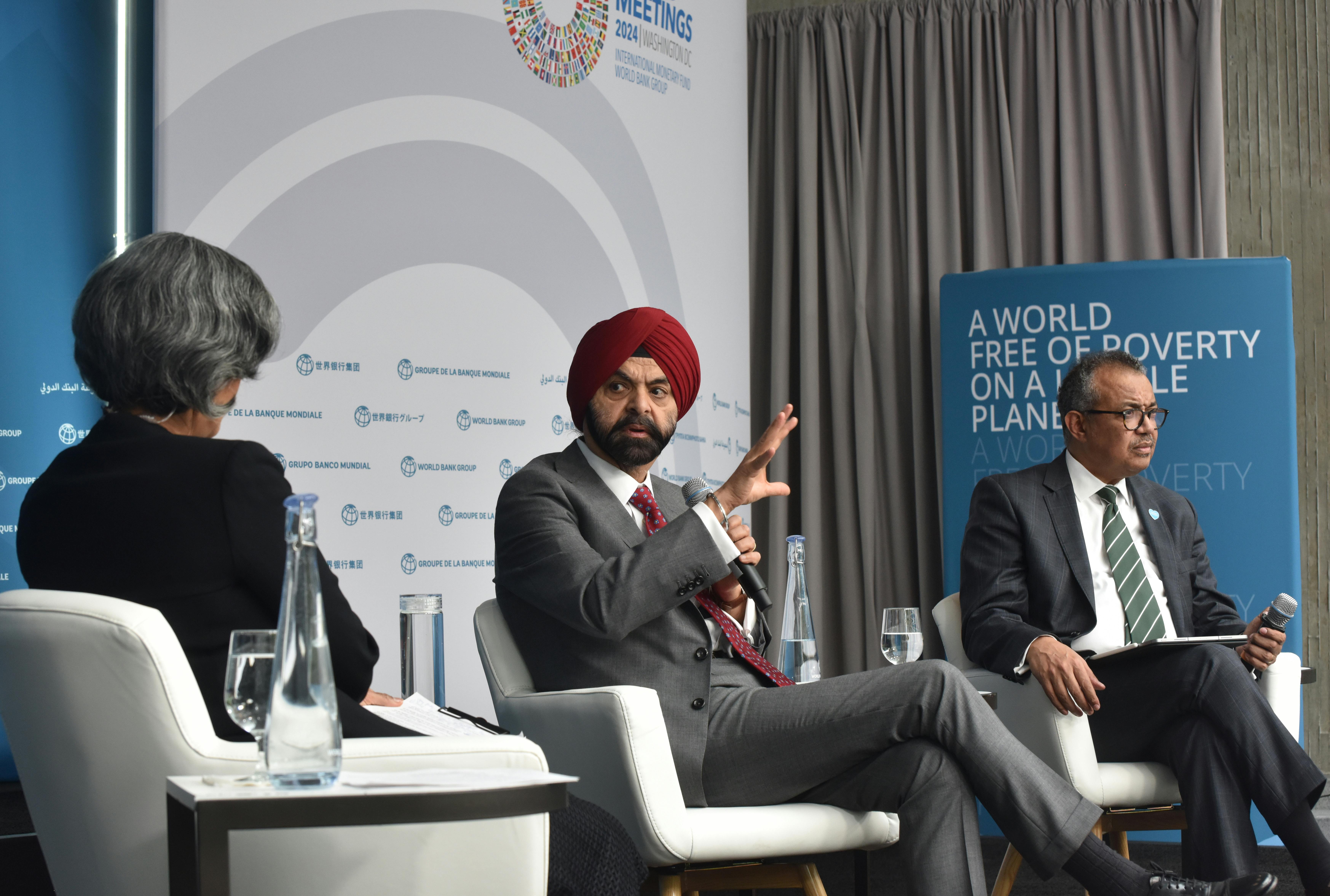 Three people sit in armchairs on a dais while talking.