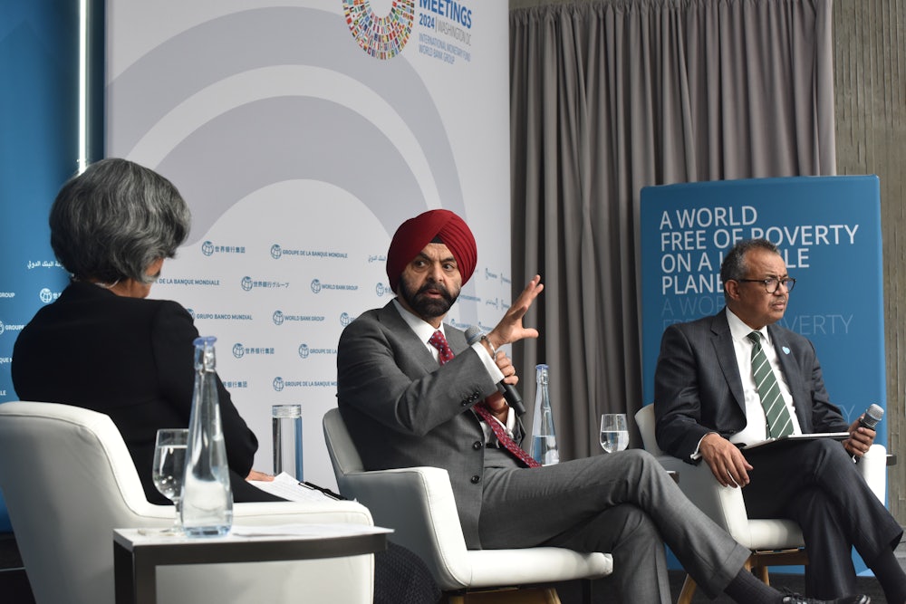 Three people sit in armchairs on a dais while talking.