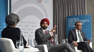 Three people sit in armchairs on a dais while talking.