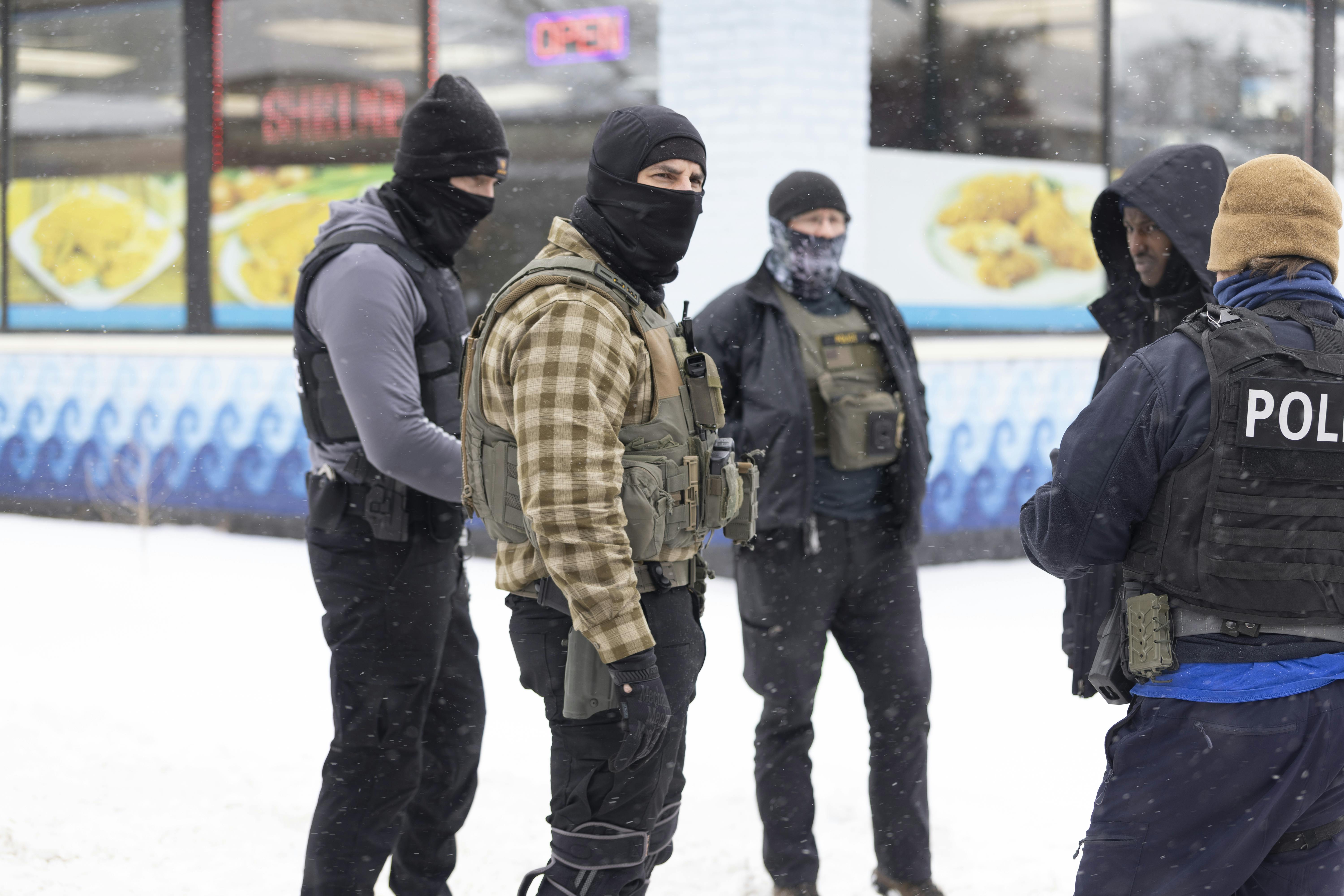 Masked ICE agents stand in the snow questioning a Black man.