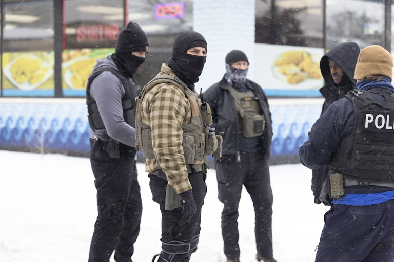 Masked ICE agents stand in the snow questioning a Black man.