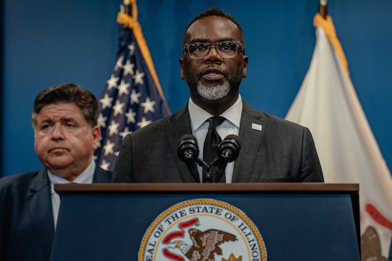 Chicago Mayor Brandon Johnson speaks at the podium with Illinois Governor JB Pritzker standing behind him.