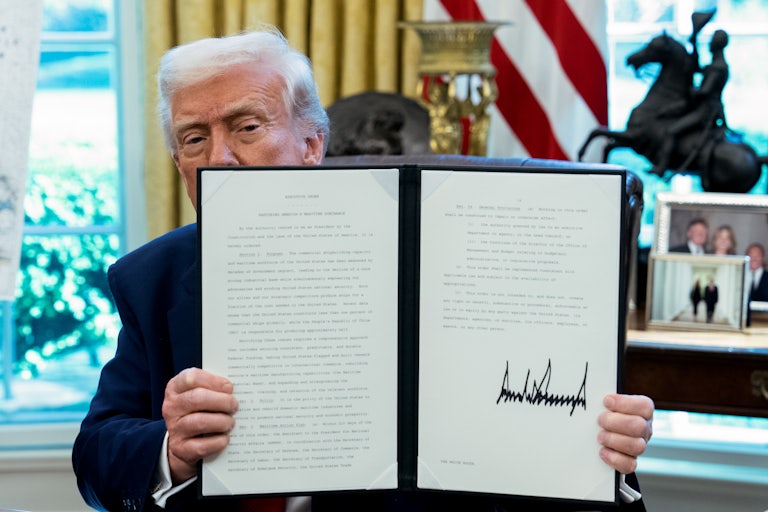 Donald Trump holds up a signed executive order while sitting in the Oval Office