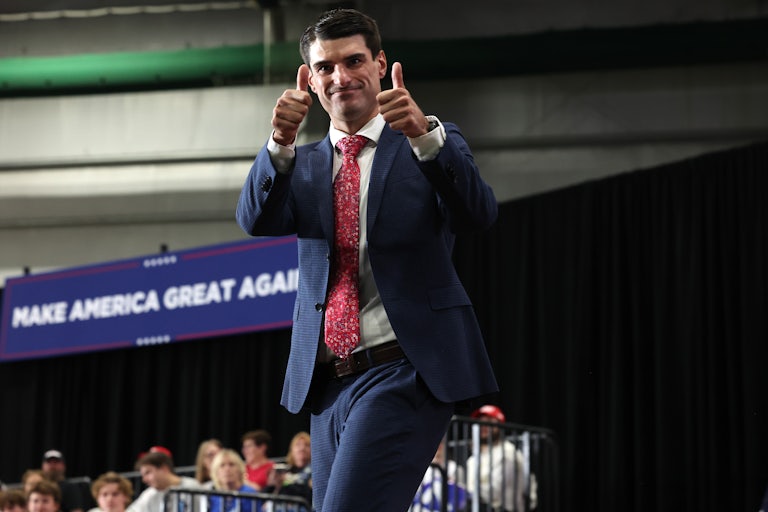Representative Robert Bresnahan smiles on stage and gives two thumbs up to the camera. A large "Make America Great Again" banner is in the background.