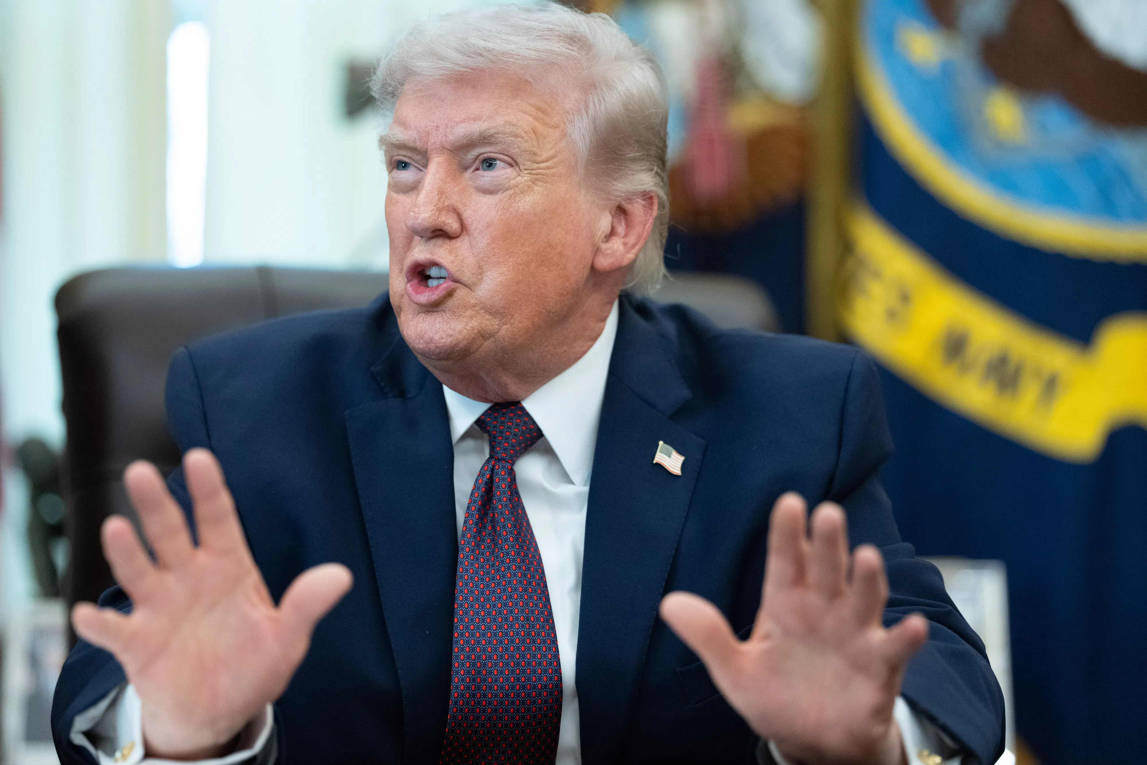 Donald Trump gestures and speaks while sitting at his desk in the Oval Office