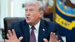 Donald Trump gestures and speaks while sitting at his desk in the Oval Office