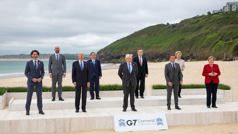 G7 leaders pose, spaced, on a platform in front of the sea.