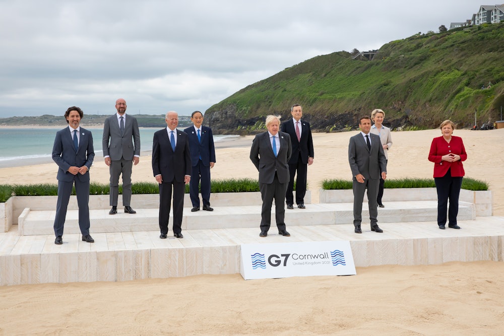 G7 leaders pose, spaced, on a platform in front of the sea.