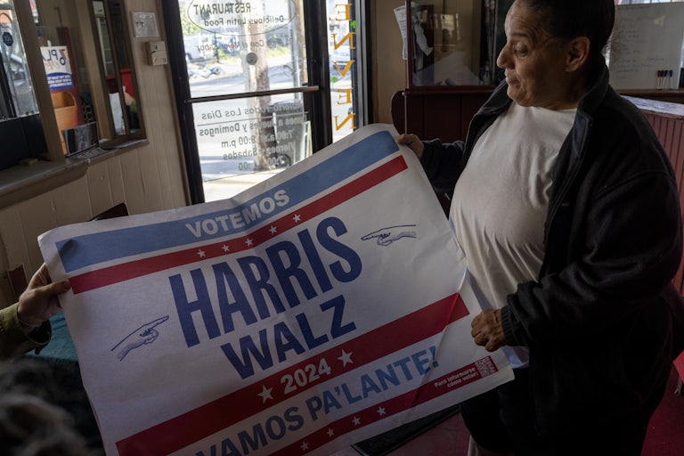A man holds a large sign that says Votemos Harris Walz