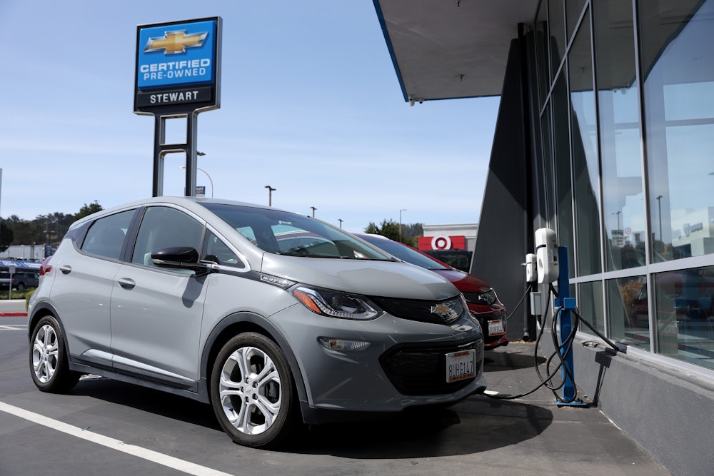 A Chevrolet Bolt sits in front of a charging station.