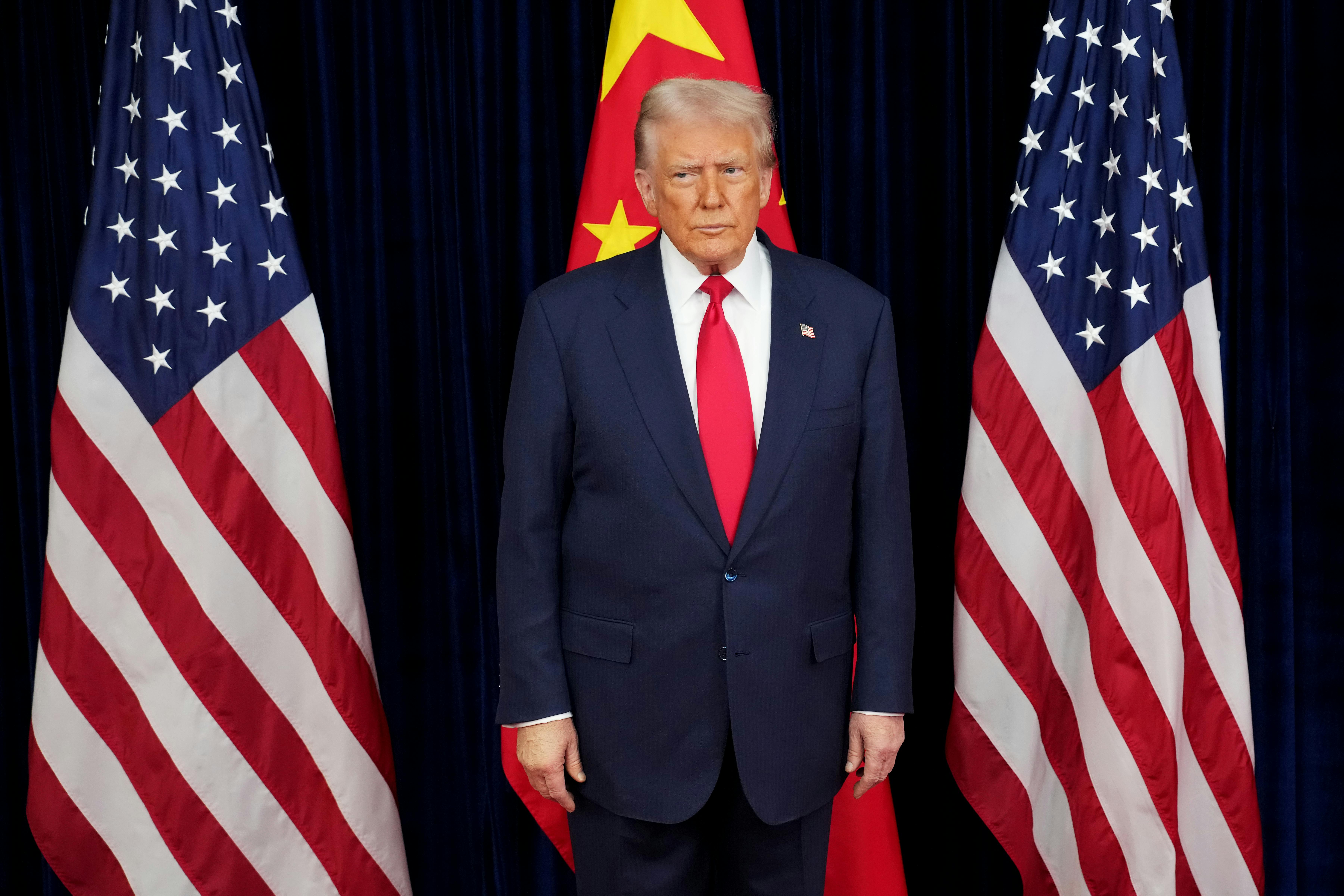 Donald Trump stands in front of two American flags and one Chinese flag