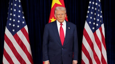 Donald Trump stands in front of two American flags and one Chinese flag
