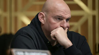 Senator John Fetterman presses his hand over his mouth while sitting in a Senate committee hearing