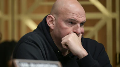 Senator John Fetterman presses his hand over his mouth while sitting in a Senate committee hearing