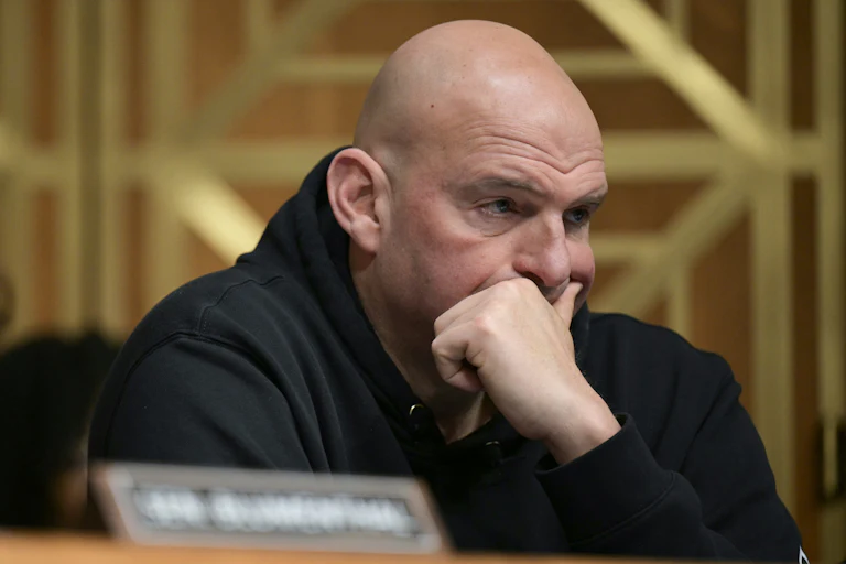Senator John Fetterman presses his hand over his mouth while sitting in a Senate committee hearing