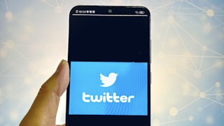 Hand holding a phone that says "Twitter" and has the bird lgoo