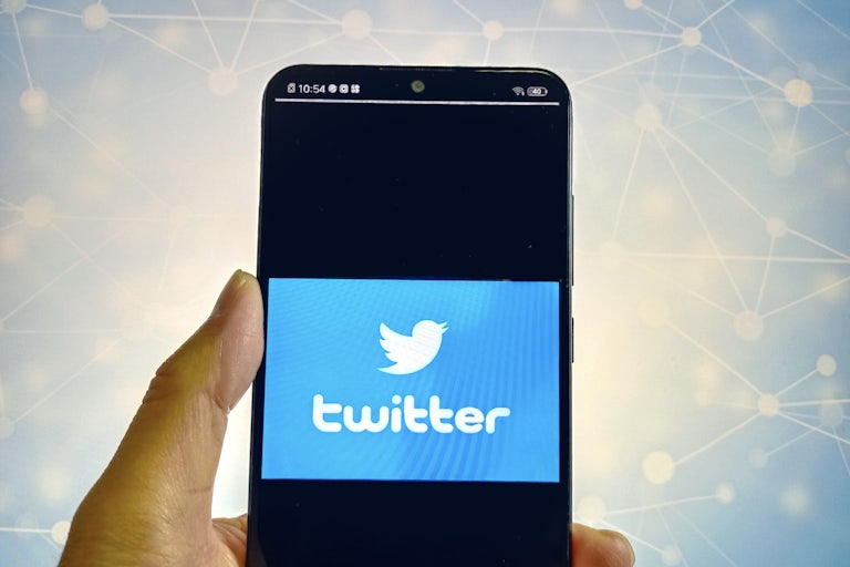 Hand holding a phone that says "Twitter" and has the bird lgoo