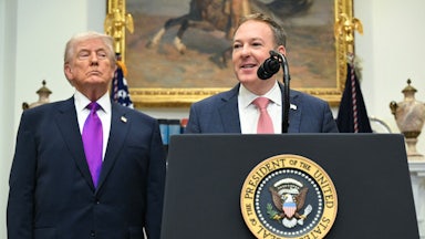 Zeldin stands at a podium, speaking, while Trump stands behind him and to the left.