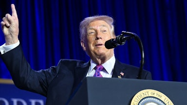 Donald Trump raises a finger above his head while speaking at a podium