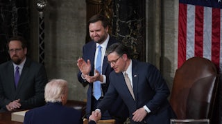 House Speaker Mike Johnson shakes hands with Donald Trump at the lectern after the State of the Union. Vice President JD Vance stands next to Johnson and claps
