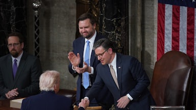 House Speaker Mike Johnson shakes hands with Donald Trump at the lectern after the State of the Union. Vice President JD Vance stands next to Johnson and claps