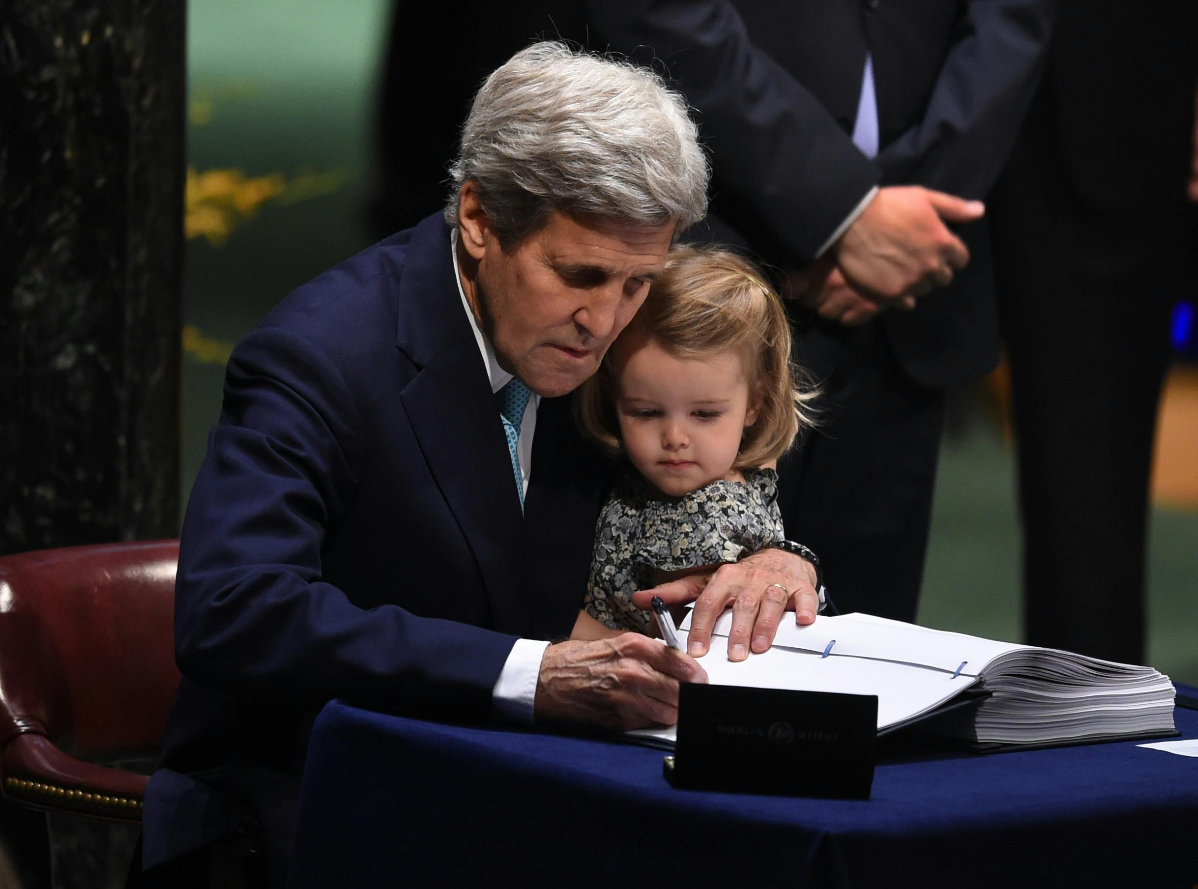 John Kerry holds his granddaughter while signing a Paris Agreement document.