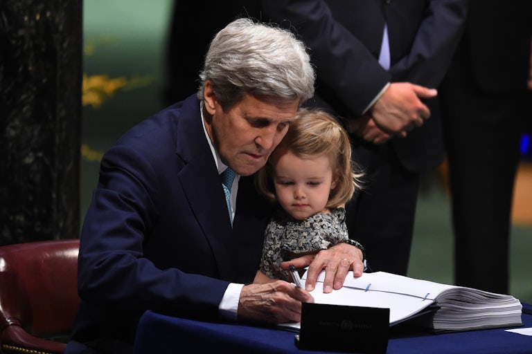 John Kerry holds his granddaughter while signing a Paris Agreement document.