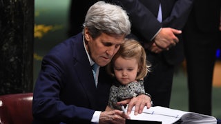 John Kerry holds his granddaughter while signing a Paris Agreement document.