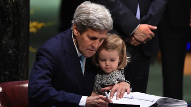 John Kerry holds his granddaughter while signing a Paris Agreement document.