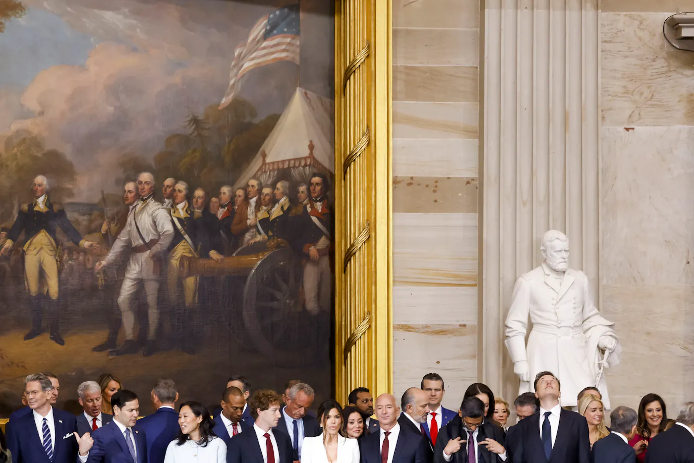 A photograph beneath towering images of the past—the painting entitled Surrender of General Burgoyne (left) and a marble sculpture of Ulysses S. Grant—at the United States Capitol, American power players of the current era gathered at Donald Trump’s second inauguration in January 2025. Among them, from left: Scott Bessent, Marco Rubio, Priscilla Chan and husband Mark Zuckerberg, Robert F. Kennedy Jr., Lauren Sánchez, Kash Patel, Jeff Bezos, Howard Lutnick, Pete Hegseth, Sundar Pichai, and Elon Musk.