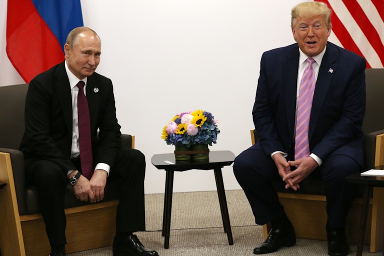 Donald Trump and Vladimir Putin sit on chairs next to each other.