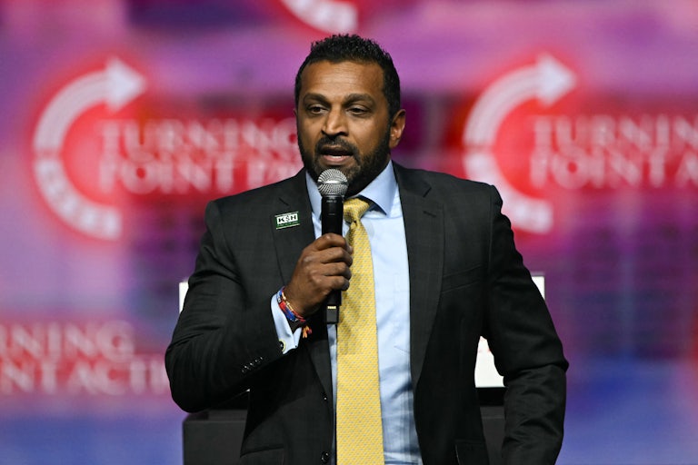 Kash Patel holds up a microphone and speaks into it