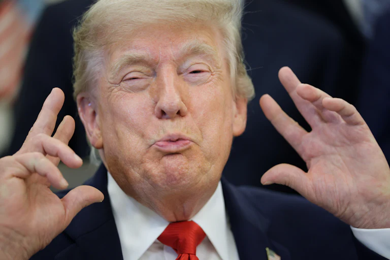 Donald Trump holds his hands next to his face and makes a weird face while sitting at his desk in the Oval Office