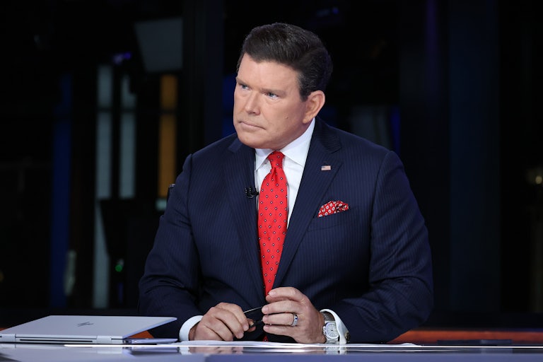 A man sitting at a desk wears a blue suit and a red tie
