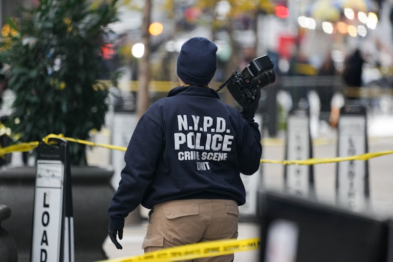 An NYPD police officer takes photos at the scene of the UnitedHealthcare shooting