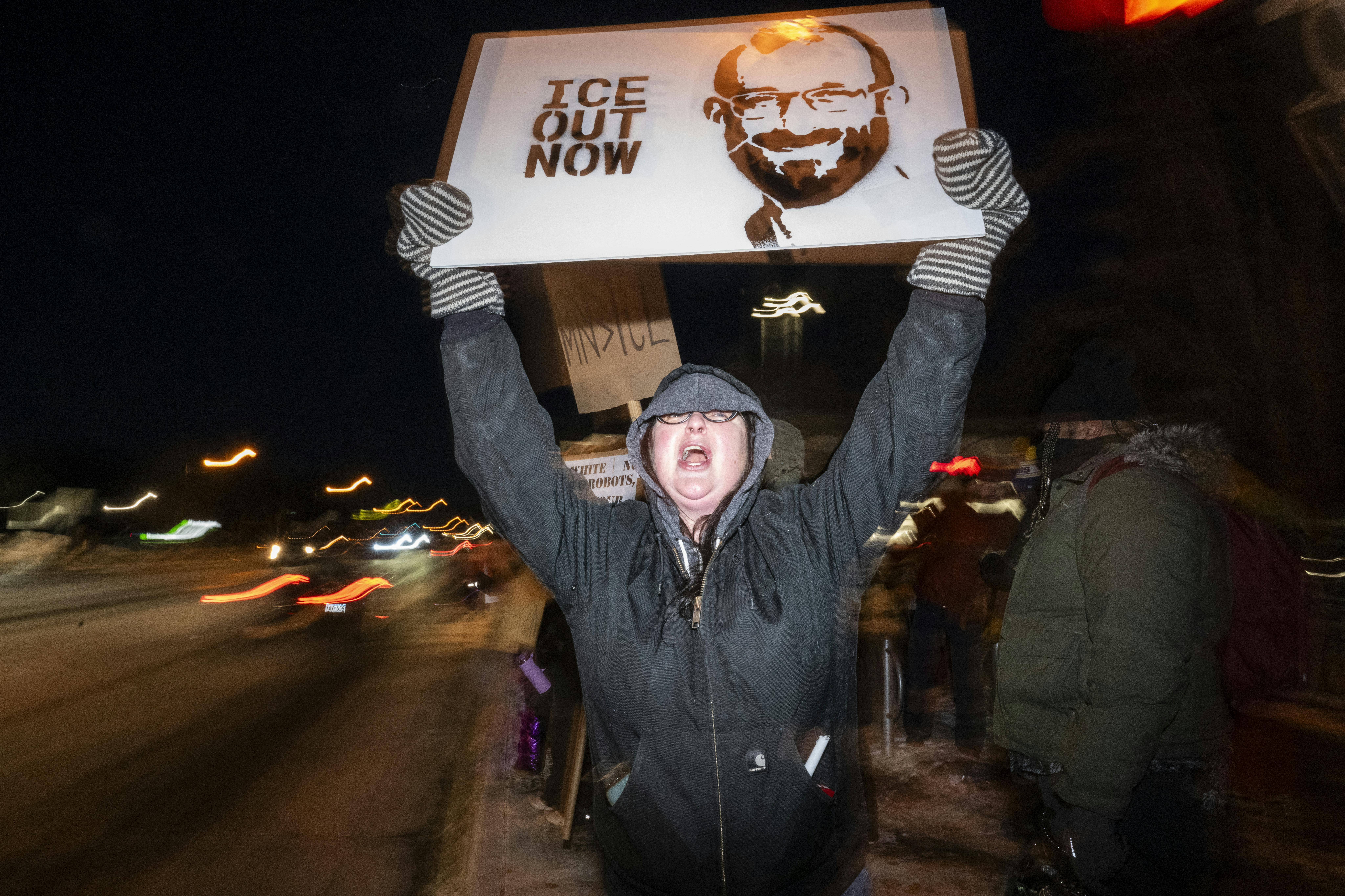 A person holds a sign that says, "ICE out" with a photo of Alex Pretti