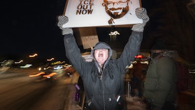 A person holds a sign that says, "ICE out" with a photo of Alex Pretti
