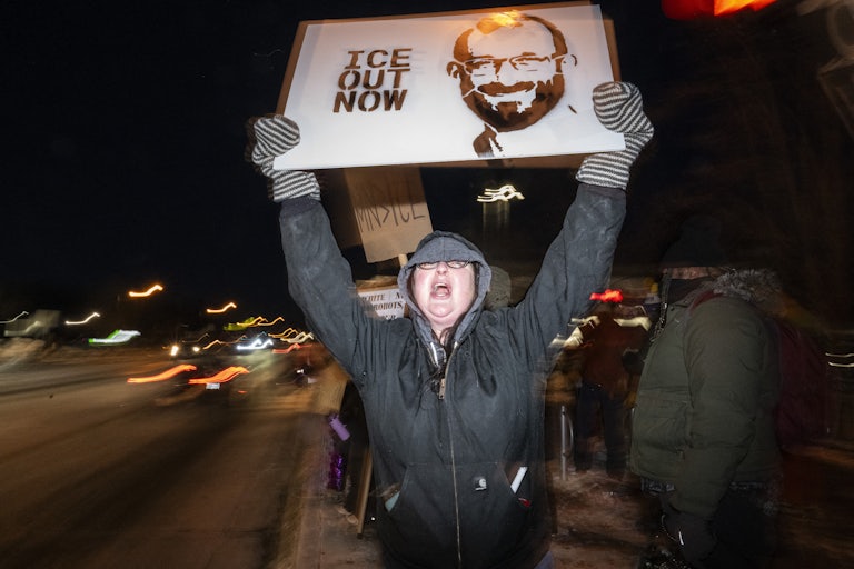 A person holds a sign that says, "ICE out" with a photo of Alex Pretti