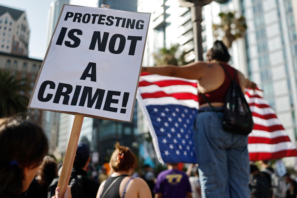 someone holds a sign reading protesting is not a crime sign while another holds up an upside down American flag