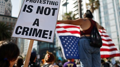 someone holds a sign reading protesting is not a crime sign while another holds up an upside down American flag