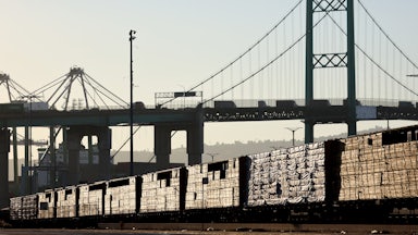Loaded freight cars sit beneath a bridge.