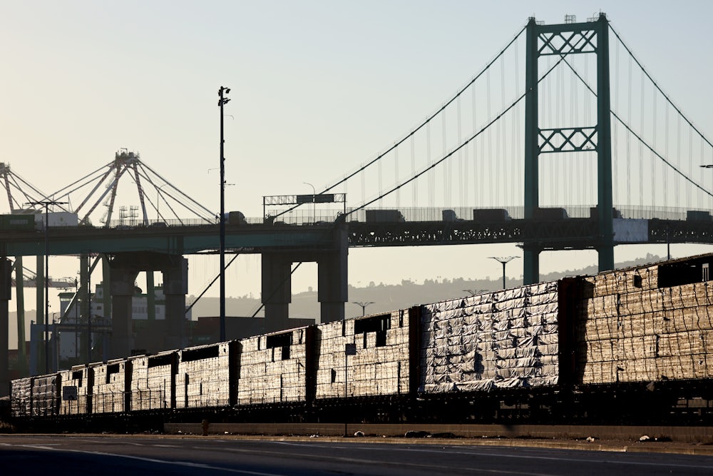 Loaded freight cars sit beneath a bridge.